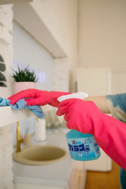 A person wearing a grey sweater, black pants, and white shoes is engaged in domestic cleaning inside a modern living room. They are using a mop to clean a light-colored, smooth tile floor that appears